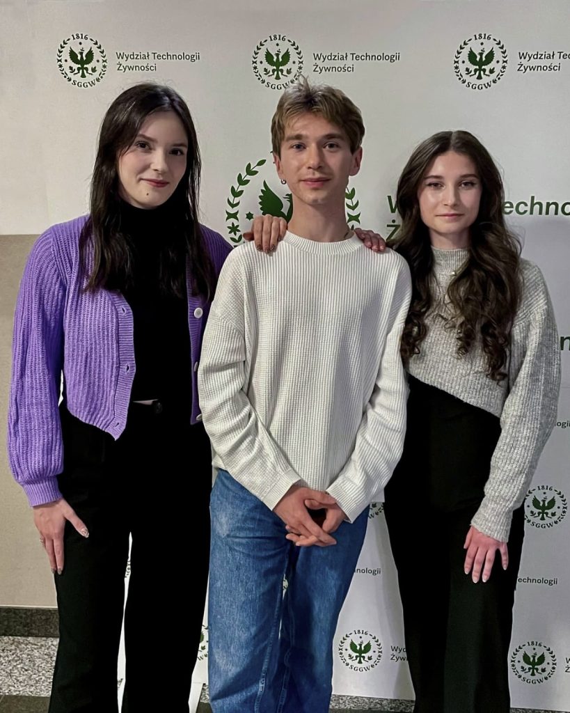 Dwie studentki oraz student stoją na tle ścianki z napisem Wydział Technologii Żywności